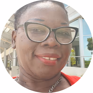 Smiling woman wearing black cat-eye glasses and hoop earrings outdoors in front of a building.