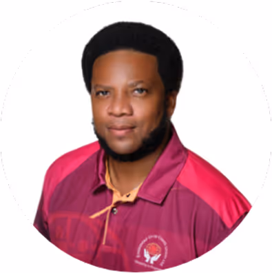 Man with short afro and beard wearing a maroon and pink collared shirt against a white background.